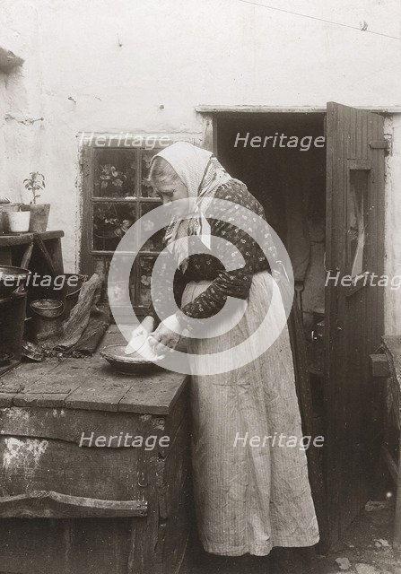 A woman in apron and headscarf washing up a mug outside her home, Landskrona, Sweden, 1910. Artist: Unknown