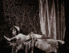 A young woman, posing semi-naked in a photographic studio, lying full-length on a fur..., c1900. Creator: Unknown.