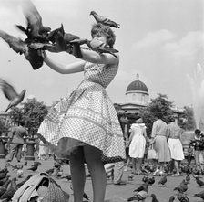 A woman in a gingham dress feeding the pigeons in Trafalgar Square, London c1946-c1959. Artist: John Gay