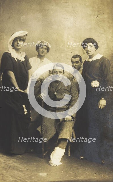 Four soldiers posing, three in drag, with an injured soldier seated in the centre, [1910-1919?]. Creator: Unknown.