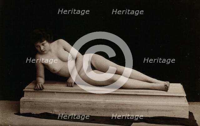 A young woman posing naked in a photographic studio, lying on a wooden plinth, approx 1900. Creator: Unknown.