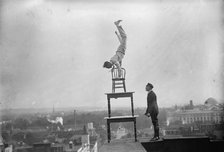 J. Reynolds, Performing Acrobatic And Balancing Acts On High Cornice Above 9th Street, N.W., 1917. Creator: Harris & Ewing.