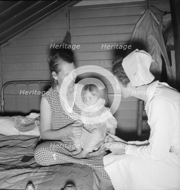Resident nurse interviews mother and examines sick baby, FSA camp, Farmersville, CA, 1939. Creator: Dorothea Lange.