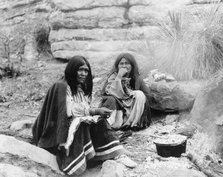 Two Apache Indian women at campfire, cooking pot in front of one, c1903. Creator: Edward Sheriff Curtis.