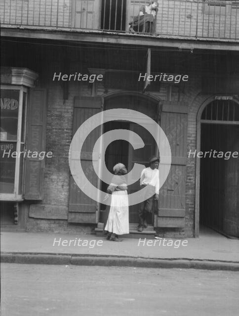 View from across street of a man and woman standing by a doorway and a woman seated...c1920-1926. Creator: Arnold Genthe.