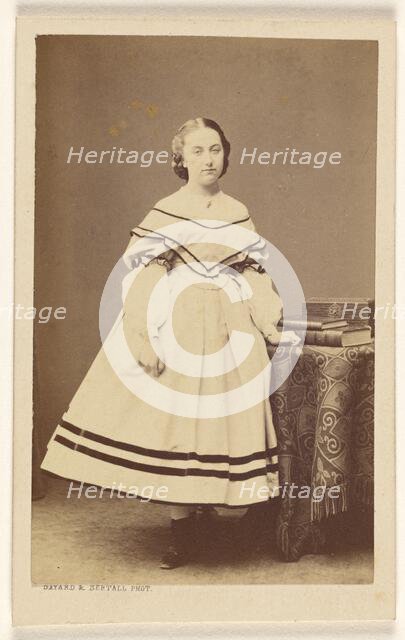 Unidentified woman standing near a table with books on top, 1865-1875. Creator: Bayard & Bertall.