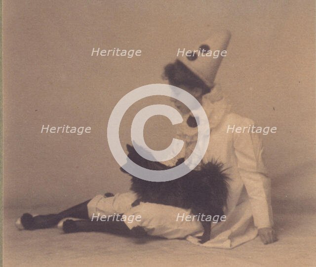 Girl dressed in a pierrot costume with a small black dog on her lap, between 1900 and 1920. Creator: Unknown.