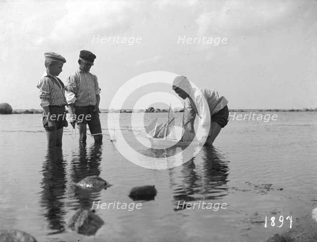 Three boys playing with a model sailing ship, 1897. Artist: Unknown