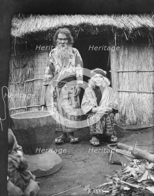 Ainu man and seated woman at the entrance of a hut, 1908. Creator: Arnold Genthe.