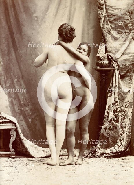 Two women posing naked in a photographic studio, standing embracing each other in front..., c1900. Creator: Unknown.