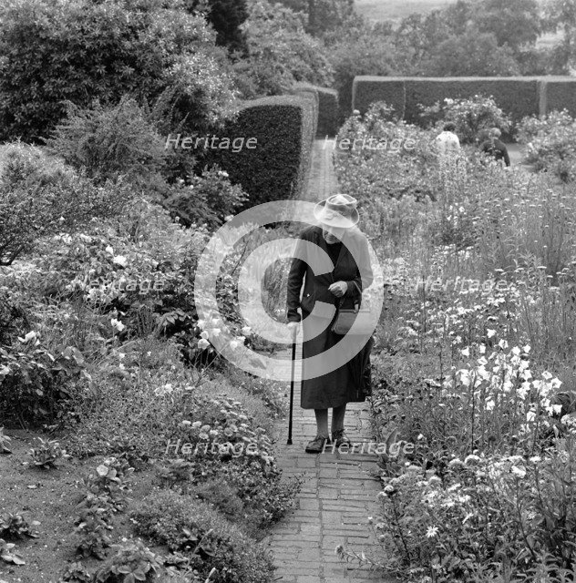 An elderly lady walking in a flower garden in Aldeburgh, Suffolk,1956. Artist: John Gay