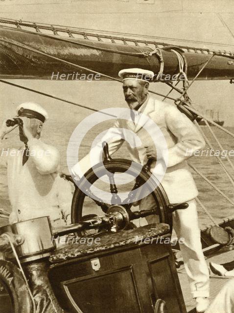 King George V at the wheel of of his yacht, Britannia, during Cowes Regatta week, 1924, (1935).   Creator: Unknown.