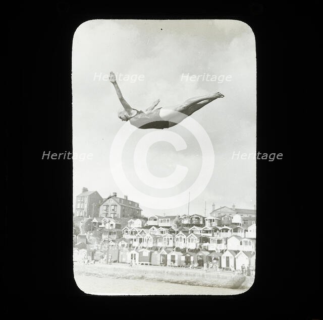 A swimmer diving into the sea at Southcliff, Walton-on-the-Naze, with beach huts on South..., 1920s. Creator: Norman Kingsley Harrison.