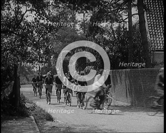 A Group of Young Female Civilians Wearing School Uniforms Riding Bicycles Along a Dusty Road, 1920. Creator: British Pathe Ltd.