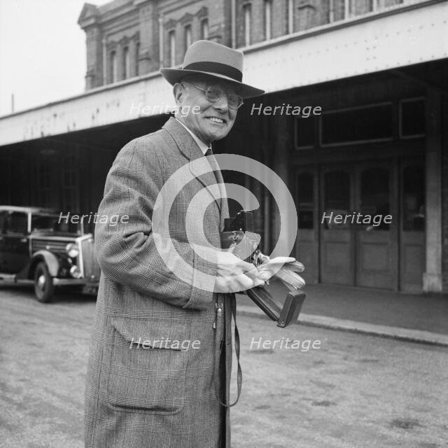 John Laing holding a Rolleiflex camera outside Bournemouth train station, 30/05/1953. Creator: John Laing plc.