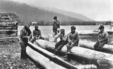 Kamchadals on the river bank near the baht and logs prepared for hollowing out the baht, 1922-1923. Creator: Rene Malaise.