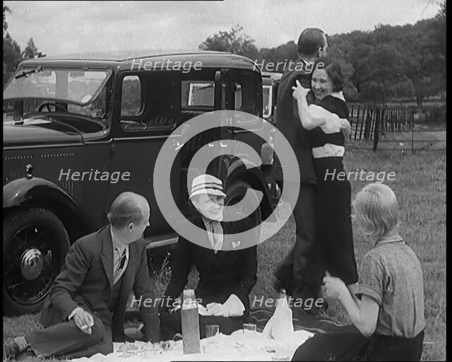 Male and Female Civilians Having a Picnic Beside a Car Whilst Two of Them Are Dancing, 1931. Creator: British Pathe Ltd.