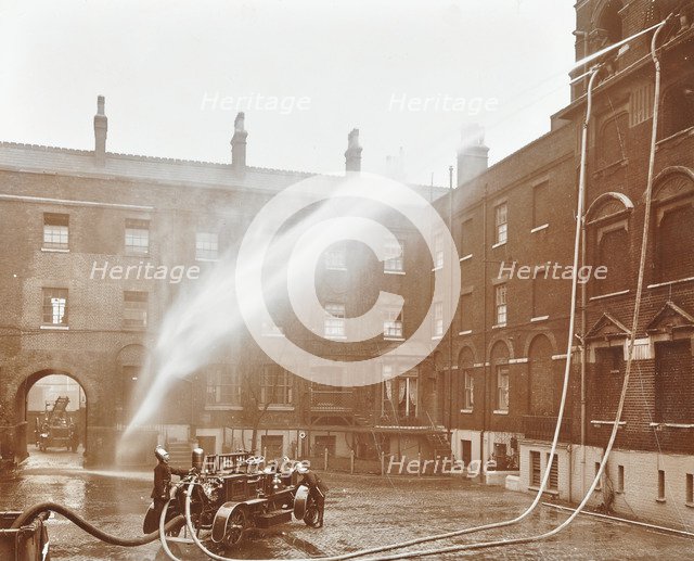 Firemen demonstrating hoses worked by a petrol motor pump, London Fire Brigade Headquarters, 1909. Artist: Unknown.