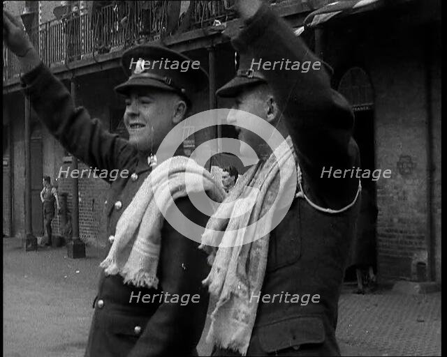 Two Uniformed British Soldiers With Arms Raised Standing Outside Brick Building, 1937. Creator: British Pathe Ltd.