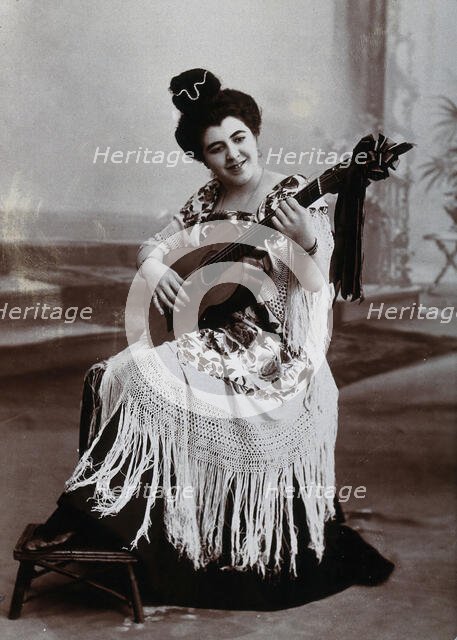 A seated woman, playing a guitar, wearing a fringed shawl, c1900. Creator: Unknown.