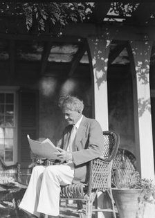 Arnold Genthe seated outdoors in a wicker chair reading, between 1911 and 1942. Creator: Arnold Genthe.