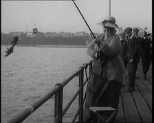 Female Civilian Wearing a Hat with a Dark Ribbon Fishing from a Pier, 1920. Creator: British Pathe Ltd.