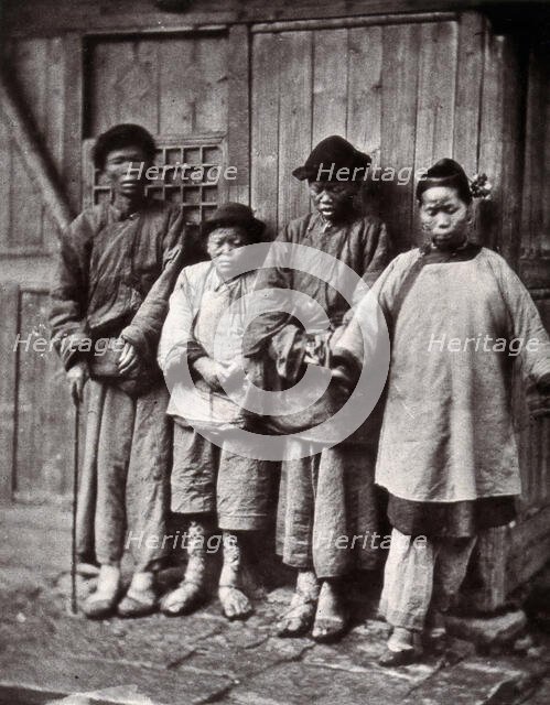 Foochow, China: four people with leprosy, wearing thick clothing, standing outside a wooden..., 1873 Creator: John Thomson.