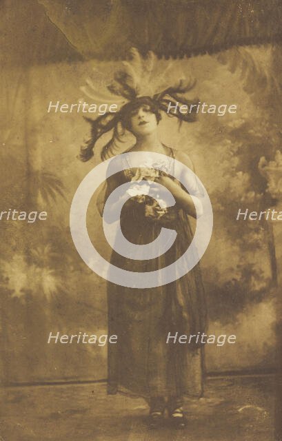 A performer in drag poses on stage wearing a head garment with sprawling feathers, [1910-1919?]. Creator: Unknown.