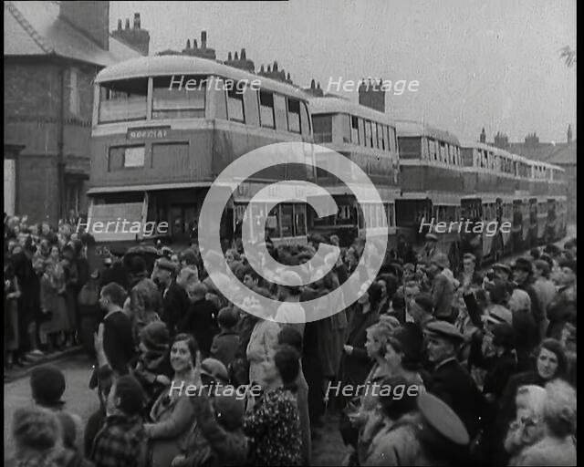 Men, Women, and Children Standing by a Line of Buses Parked in a Residential Street, 1939. Creator: British Pathe Ltd.