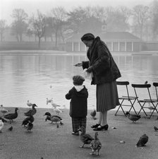 Woman and a young boy feeding the ducks and birds on the edge of the Serpentine, Hyde Park, 1960-70. Creator: John Gay.