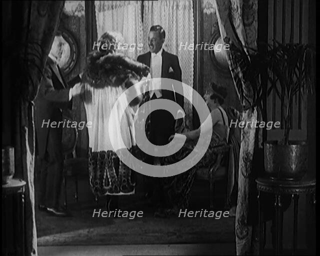 A Male Civilian Helping a Female Civilian Remove Her Fur Trimmed Coat Revealing an Ornated Gown, 192 Creator: British Pathe Ltd.