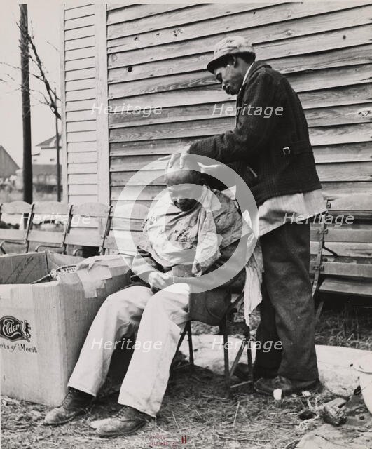 Negro getting a haircut in front of church which houses flood refugees. Sikeston, Missouri, 1937-02. Creators: Farm Security Administration, Russell Lee.