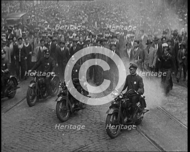 Male American Police Officers Riding Motorbikes Escorting a Large Crowd in a Parade, 1930. Creator: British Pathe Ltd.
