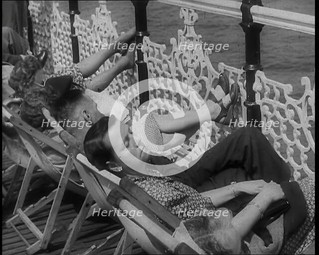 A Woman Sleeping in a Deckchair by Railings on the Promenade at Brighton With a Man and..., 1939. Creator: British Pathe Ltd.