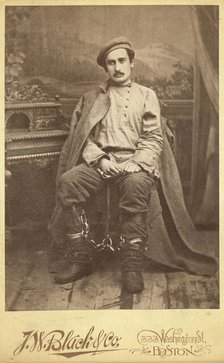 Full-length portrait of a man in convict clothing and leg irons, seated..., between 1880 and 1886. Creator: Unknown.