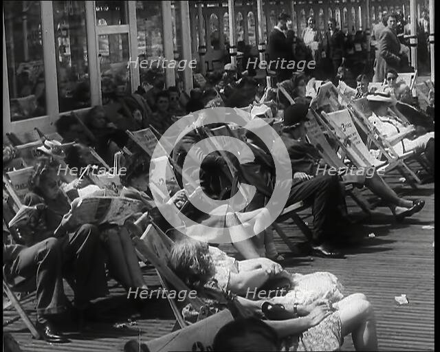 Lines of Men and Women Sitting in Deckchairs on a Pier at  Brighton With Several Reading..., 1939. Creator: British Pathe Ltd.
