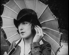 Fashionable Lady Sitting in a Garden Wearing Headphones and Carrying a Parasol, 1922. Creator: British Pathe Ltd.