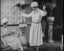 Two Female Civilians Leisuring in a Drawing Room Wearing Long Dresses and Hats Comparing..., 1920. Creator: British Pathe Ltd.