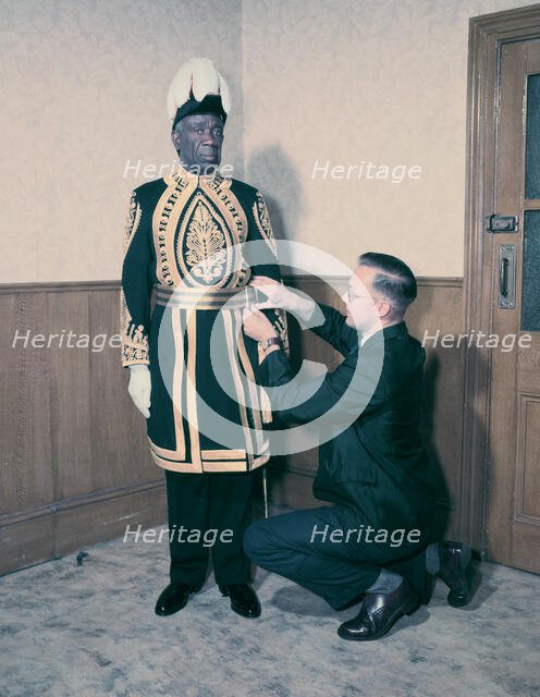 A Paramount Chief being fitted for his robes for the coronation of Queen Elizabeth II, 1953. Creator: Arthur Charles Kirby Ware.
