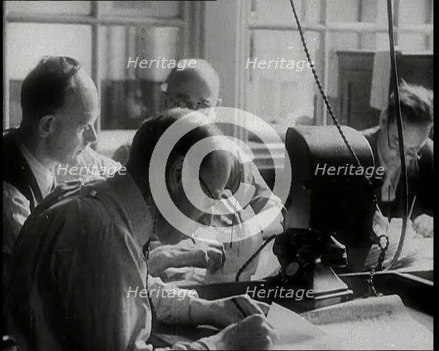 Four Male British Journalists Sitting Around a Table Covered in Papers and Writing, 1939. Creator: British Pathe Ltd.
