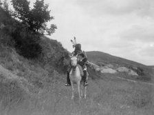 Sioux Indian on horseback, wearing two feathers, beaded buckskin shirt, and leggings..., c1907. Creator: Edward Sheriff Curtis.