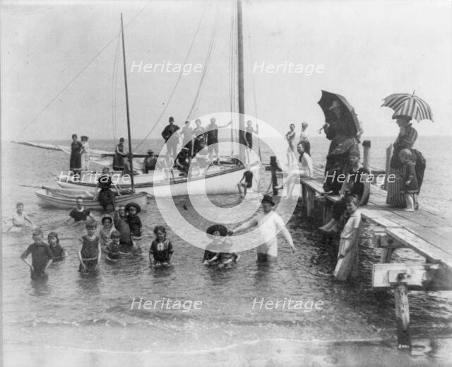 Men, women, and children in bathing suits on dock, sailboats, and in water..., c1880. Creator: Unknown.