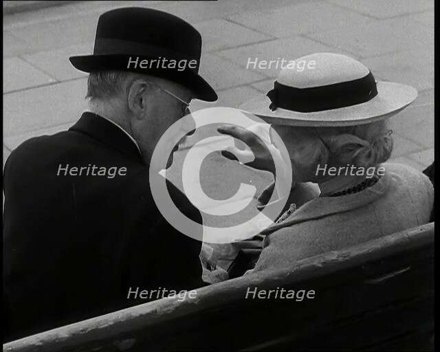 A Rear View of a Elderly Man and Woman Sitting on a Bench and Talking, Both Wearing Hats..., 1938. Creator: British Pathe Ltd.