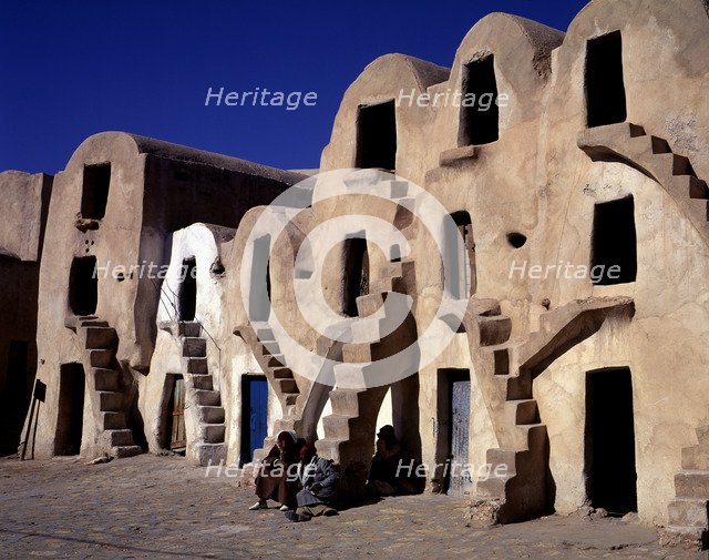 Old typical barns with people sitting on the stairs.