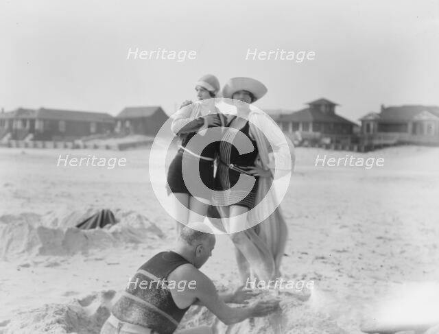 Unidentified man building sand castle and two women, Long Beach, New York, between 1911 and 1942. Creator: Arnold Genthe.