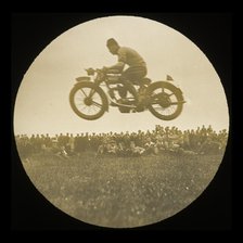 A view of a motorcycle jumping in front of a crowd of onlookers at an unknown..., 1920s-1930s.  Creator: Norman Kingsley Harrison.