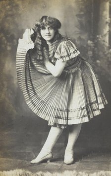 An amateur actor in drag holds up his impressive folded dress to one side, (between 1910 and 1919?). Creator: Unknown.