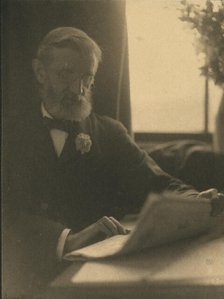 Bearded man in spectacles reading a newspaper, c1900. Creator: Anne K Pilsbury.