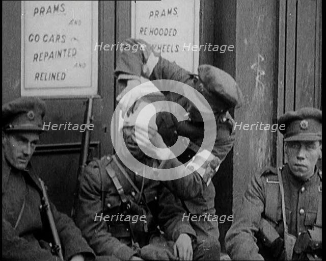 Irish Soldiers Sitting in the Street and Tending to Their Injuries from Fighting in Dublin, 1922. Creator: British Pathe Ltd.