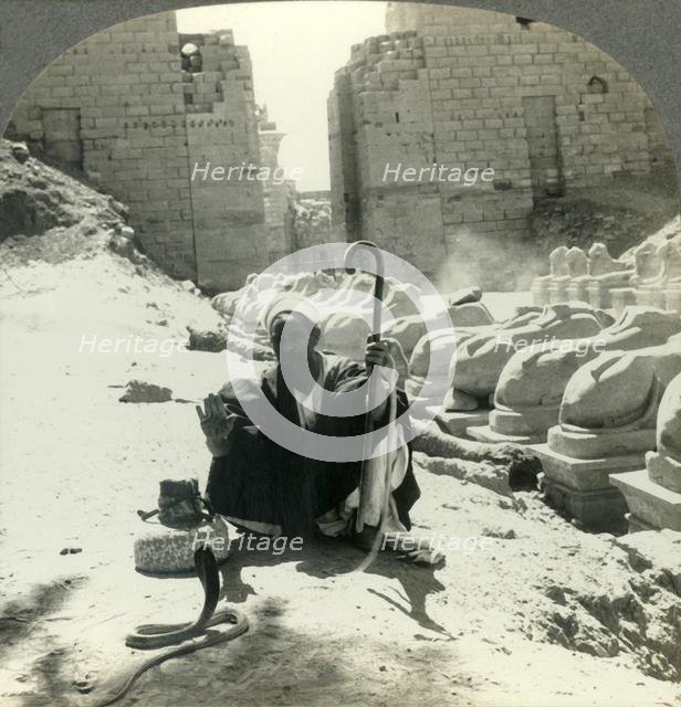 'An Egyptian Snake Charmer Piles His Trade Beside the Avenue of Sphinxes, Temple of Karnak, Thebes,  Creator: Unknown.